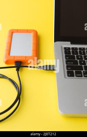 Disque dur externe sur fond jaune connecté au port USB d'un ordinateur portable Banque D'Images