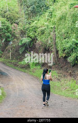 belle fille latine marchant le long d'un sentier au milieu d'une forêt en colombie. capture des photos de la nature avec son téléphone cellulaire. influenceur marchant Banque D'Images