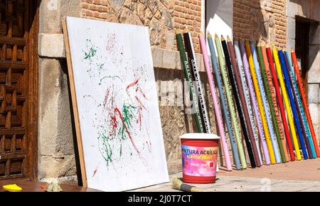 Crayons de couleur géants reposant sur un mur d'une maison à côté d'un pot de peinture géant et d'une toile avec des traits de couleur Banque D'Images