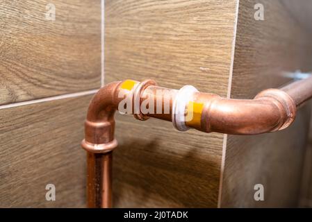 Coude de tuyau en cuivre pour les installations au gaz naturel, fixé à un mur dans une chaufferie bordée de carreaux de céramique. Banque D'Images