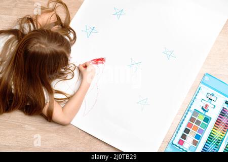 Un petit garçon dessine une photo sur le sol dans sa chambre, vue de dessus. Art des enfants , école à domicile et concept de créativité. Photo de haute qualité. Banque D'Images