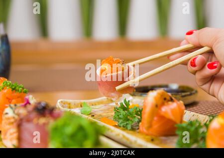 Femme mangeant de délicieux sushi gunkan, en gros plan sur des baguettes Banque D'Images