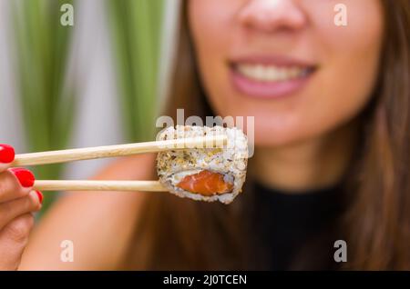 Femme mangeant de délicieux sushi gunkan, en gros plan sur des baguettes Banque D'Images