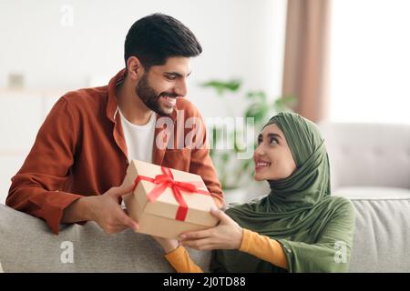 Un mari musulman donne une boîte cadeau à une femme heureuse assise à l'intérieur Banque D'Images