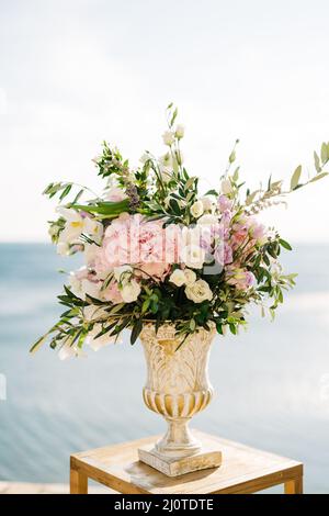 Bouquet de fleurs dans un vase antique se dresse sur un tabouret sur fond d'eau Banque D'Images