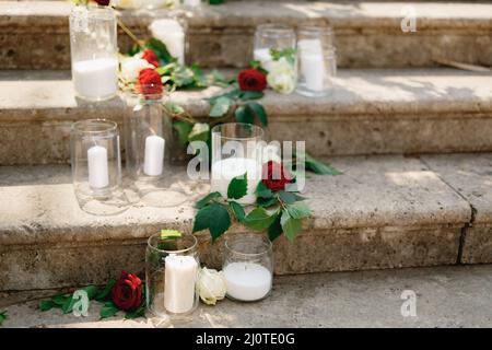 Des bougies blanches dans des pots en verre entourés de roses se tiennent sur des marches en pierre Banque D'Images