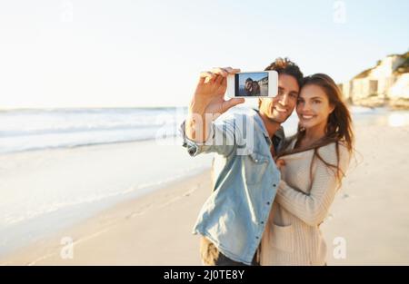 J'adore la plage. Photo d'un jeune couple affectueux prenant un selfie à la plage. Banque D'Images