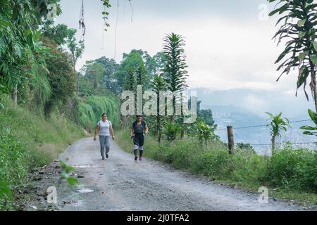 Mère et fille marchant le long d'une route de terre (trocha) au sommet d'une montagne colombienne dans la région du café près de la ville de Pereira-Colombie, entourent Banque D'Images