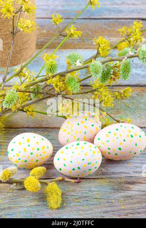 Composition de Pâques de brindilles de saule en fleurs, de bois de chien et d'oeufs de Pâques avec un motif de points jaunes et verts sur un rétro en bois Banque D'Images