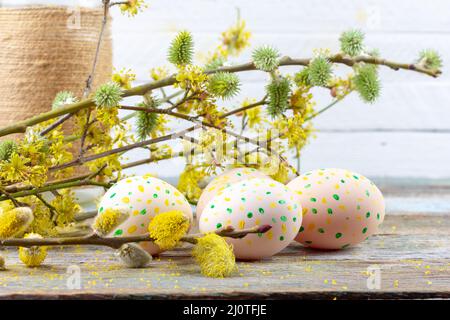 Composition de Pâques de brindilles de saule en fleurs, de bois de chien et d'oeufs de Pâques avec un motif de points jaunes et verts sur un rétro en bois Banque D'Images