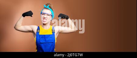 Jeune belle femme caucasienne ouvrier réparateur avec les yeux bleus en uniforme montrant les muscles du bras, fièrement sourire et faisant une str Banque D'Images