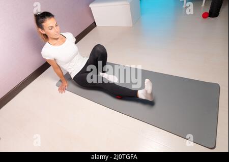 Femme sportive fine caucasienne faisant l'auto-massage sur le tapis de fitness avec ballon de massage à l'intérieur. Massage auto-isolation Banque D'Images