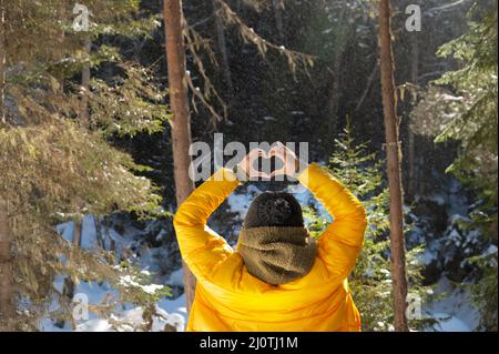 Portrait arrière jeune femme caucasienne et montre les doigts geste de coeur, l'amour au niveau des yeux. Vue arrière en forêt Banque D'Images