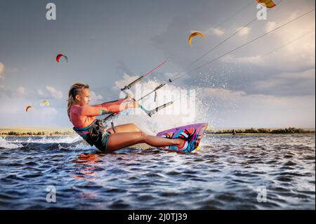 Kitesurfer professionnel jeune femme caucasienne glisse sur un plateau le long de la surface de la mer au coucher du soleil sur fond de beauffu Banque D'Images