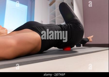 Gros plan jeune femme caucasienne effectuant un auto-massage myofascial de sa cuisse et des fesses avec une boule de massage sur un tapis de massage. 4k Banque D'Images