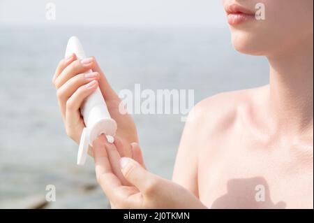La jeune femme caucasienne met de la crème solaire à portée de main sur le fond de la mer par une journée ensoleillée Banque D'Images