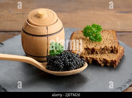 Caviar de paddlefish noir granuleux frais en cuillère en bois marron sur une table brune, gros plan Banque D'Images