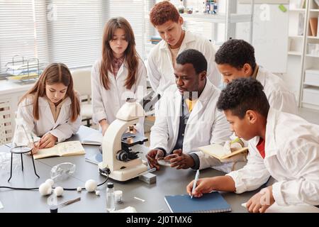 Portrait d'un groupe diversifié d'enfants faisant des expériences avec un enseignant en laboratoire de chimie scolaire Banque D'Images