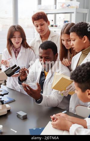 Portrait vertical d'un groupe diversifié d'enfants faisant des expériences avec un enseignant en laboratoire de chimie scolaire Banque D'Images