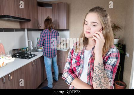 Appel important. Une jeune femme caucasienne avec un visage abattu sérieux parle au téléphone tout en se tenant de nouveau dans la cuisine Banque D'Images