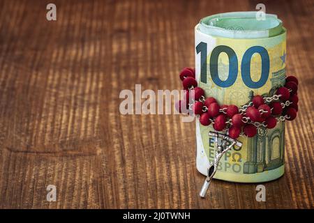 Rosaire catholique avec perles et rouleau de monnaie européenne sur une table en bois brun foncé Banque D'Images