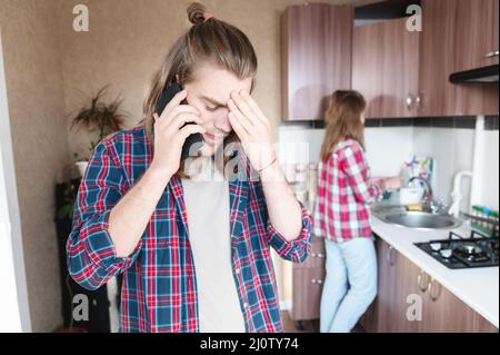 Perturbation grave jeune homme aux cheveux longs debout dans la cuisine utilise son téléphone portable ou commander un service sur le tal Internet Banque D'Images