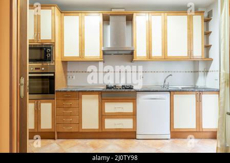 cuisine avec mobilier en bois et tiroirs assortis avec comptoir en pierre grise et appareils blancs avec sol en grès clair Banque D'Images