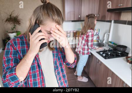 Perturbation grave jeune homme aux cheveux longs debout dans la cuisine utilise son téléphone portable ou commander un service sur le tal Internet Banque D'Images