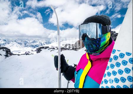 Portrait d'une fille skieuse dans une veste multicolore brillante dans un masque de ski avec son visage fermé lors d'une journée ensoleillée sur fond Banque D'Images