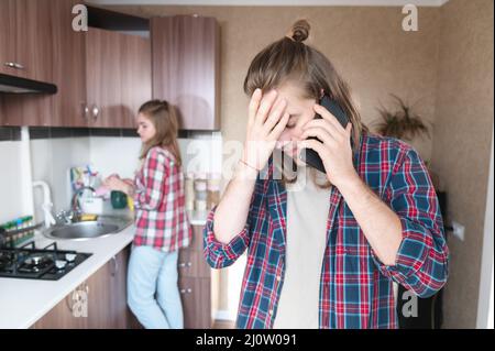 Perturbation grave jeune homme aux cheveux longs debout dans la cuisine utilise son téléphone portable ou commander un service sur le tal Internet Banque D'Images