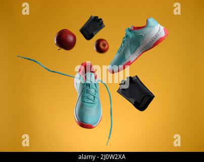 Pomme rouge, gants et paire de sneakers en tissu bleu avec lacets levitent sur fond jaune. Banque D'Images