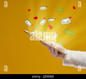 La main femelle tient une tablette avec des coeurs, des dialogues et des lettres volant sur un fond jaune. Dépendance aux médias sociaux, séquestre Banque D'Images