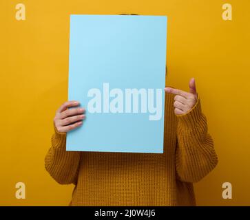 Femme dans un chandail orange tient une feuille de papier vierge sur un fond jaune. Place pour une inscription, publicité, informaa Banque D'Images