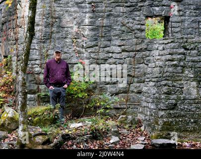 L'homme se tient à côté des ruines du moulin de Mitchell dans le terrain de loisirs de Blanchard Springs. Il porte une chemise violette et sourit. Banque D'Images