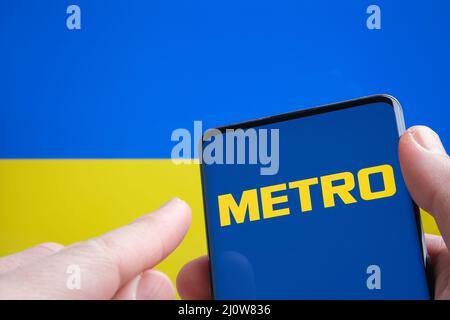 LOGO DE LA SOCIÉTÉ METRO Cash and Carry sur le smartphone et drapeau ukrainien sur l'arrière-plan. Concept. Stafford, Royaume-Uni, 20 mars 2022 Banque D'Images