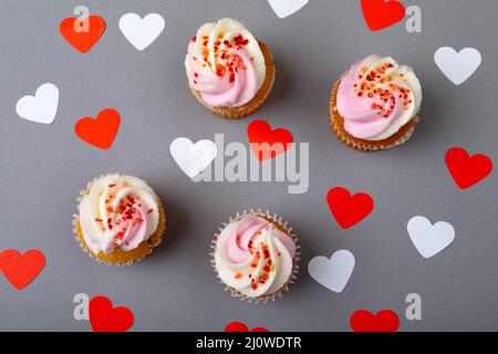 Parsemez de petits gâteaux frais au milieu de formes rouges et blanches de coeur sur fond gris Banque D'Images
