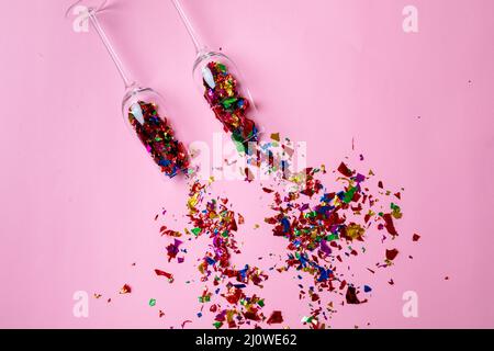 Vue en hauteur des flûtes à champagne avec des confettis multicolores éparpillés sur fond rose Banque D'Images