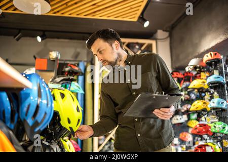 Le directeur de la boutique de vélos vérifie les informations sur le prix du casque sur la tablette, le vendeur fait un inventaire dans la boutique de sport. Thème des petites entreprises Banque D'Images