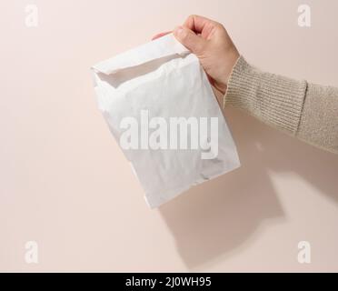 La main femelle tient un sac de papier complet sur un fond beige. Refus d'emballage en plastique, livraison de nourriture Banque D'Images