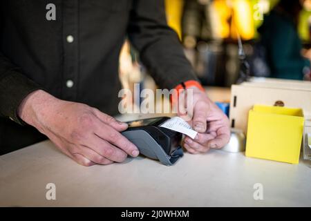 L'homme tient le terminal de paiement tout en tenant le reçu pour terminer un achat. Mains rapprochées et vue latérale. Concept de NFC, buline Banque D'Images