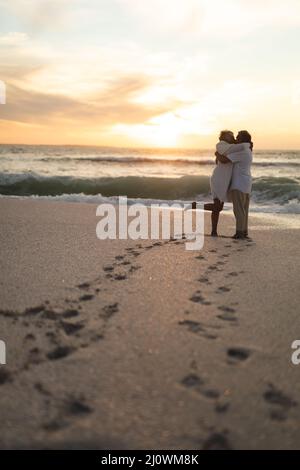 Couple biracial affectueux et nouveau, s'embrassant sur la plage au coucher du soleil Banque D'Images