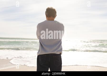 Vue arrière de l'homme biracial senior debout sur la rive regardant l'horizon au-dessus de la mer pendant la journée ensoleillée Banque D'Images