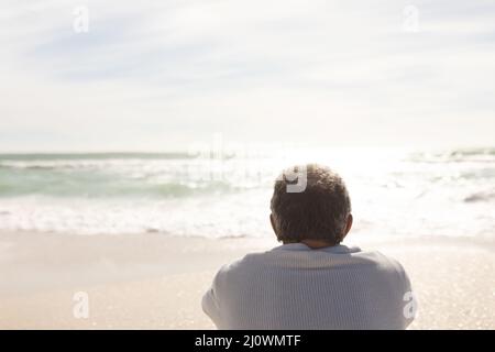 Vue arrière de l'homme biracial à la retraite regardant l'horizon sur la mer par jour ensoleillé depuis la plage Banque D'Images