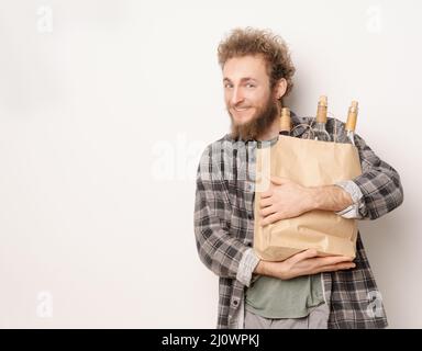 Guy tient un sac en papier avec des bouteilles de vin. Souriant, il regarde dans l'appareil photo. Concept d'un bon moment, une réunion amicale, prepas Banque D'Images