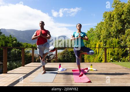 Un jeune couple afro-américain pratiquant l'arbre pose le yoga ensemble sur la terrasse le jour ensoleillé Banque D'Images