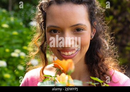 Portrait d'une jeune femme biraciale souriante avec plante à fleurs dans le jardin Banque D'Images