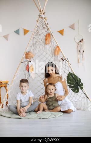 Jeune famille heureuse mère aimante avec deux enfants assis ensemble dans le tipi de wigwam à la maison Banque D'Images