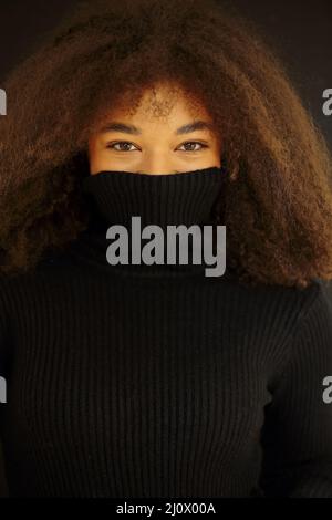 Heureuse afro-américaine curly femme avec les yeux fermés couvrant le visage avec chaud col de pull noir Banque D'Images