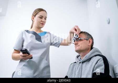 Le patient masculin subit un test oculaire et une prescription de lunettes en clinique d'ophtalmologie. Optométriste vérifiant le patient Banque D'Images