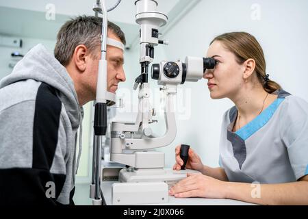 Ophtalmologiste et patient testant la vue. Homme faisant un test visuel avec optométriste. Ophtalmologiste utilisant un appareil pour l'examen des yeux Banque D'Images